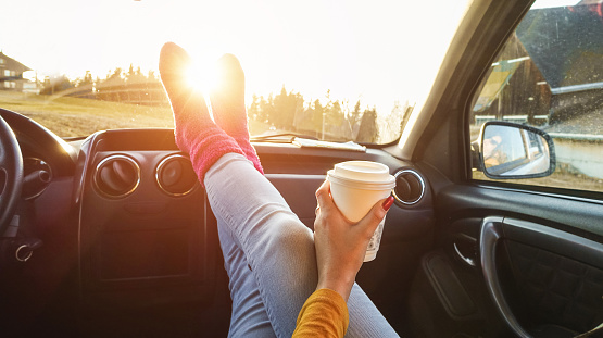 Young woman drinking coffee inside car in fall season - Girl relaxing and enjoying sunset traveling on europe mountains - Travel ,road trip and comfortable concept - Focus on paper hand