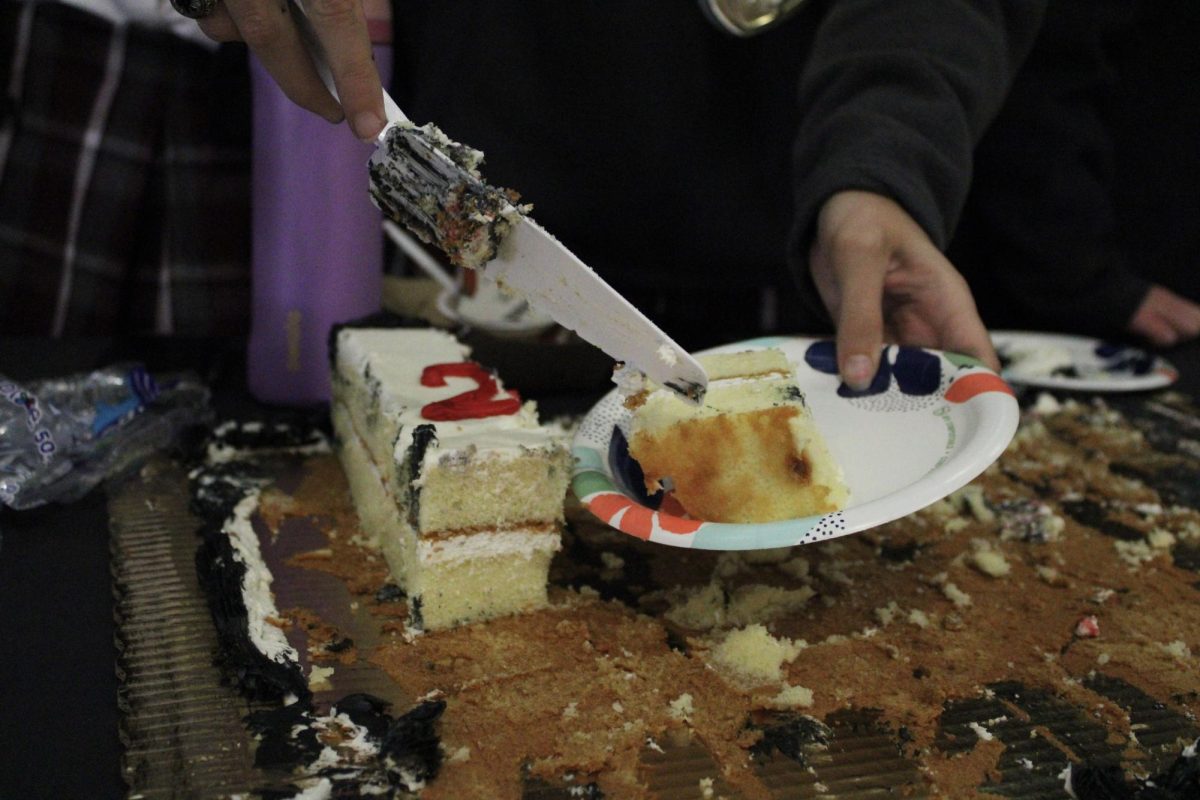 The team celebrates by cutting the celebratory cake and passing it out to students.