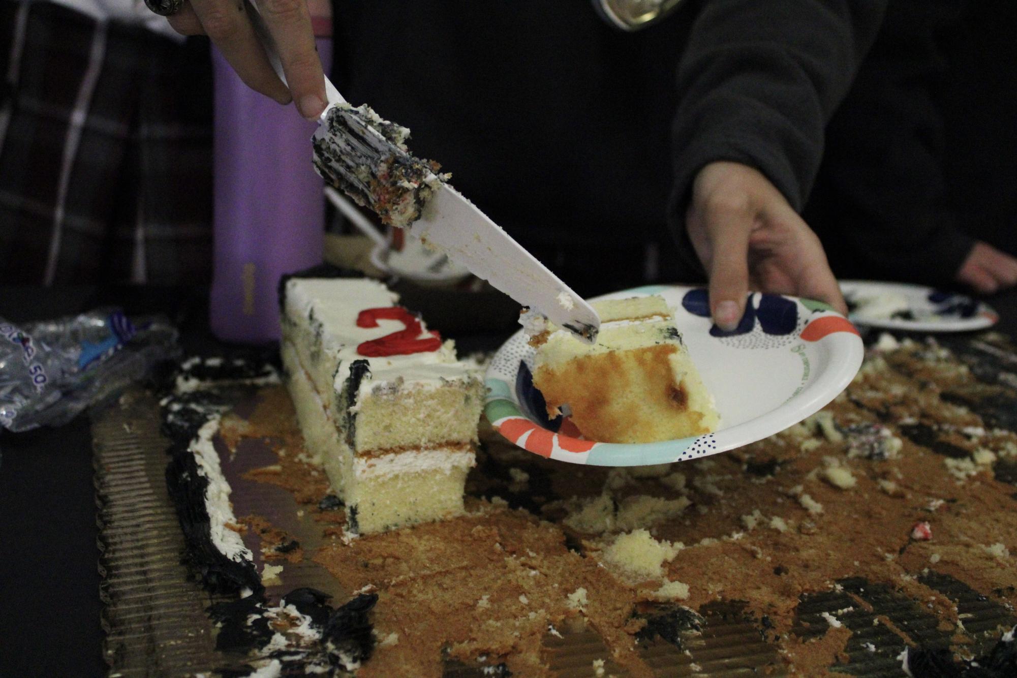The team celebrates by cutting the celebratory cake and passing it out to students.